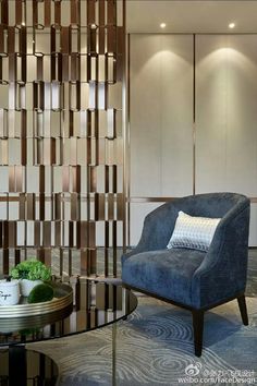 a living room with a blue chair next to a glass coffee table and wooden paneled walls