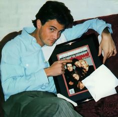 a man sitting on top of a couch holding a framed photo and looking at the camera