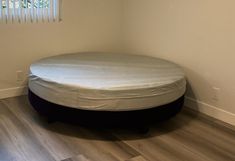 a round bed sitting on top of a hard wood floor next to a white wall