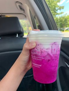 a person holding up a pink drink in the back seat of a car