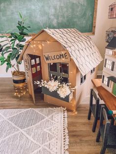 a doll house with a welcome sign on the door and flowers in front of it