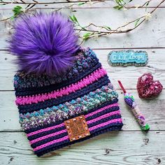 a knitted hat with purple pom - pom sitting next to it