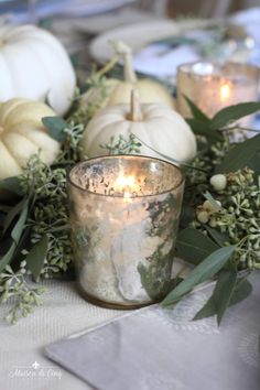 a candle is lit in front of some pumpkins and greenery on a table