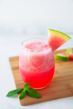 two glasses filled with watermelon and cucumber on top of a wooden cutting board