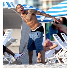 a shirtless man on the beach with his arms out in front of him and people sitting under umbrellas