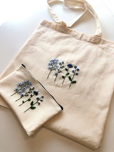 two white bags with blue flowers on them sitting on a table next to each other