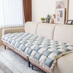 a white couch with blue and white checkerboard pattern on the back, sitting in front of a window