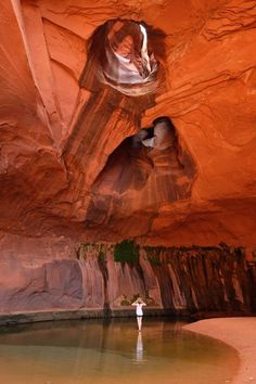 a person standing in the middle of a body of water near some rocks and cliffs