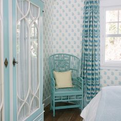 a blue chair sitting in front of a window next to a white bed and curtains