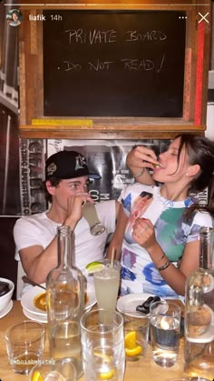 a man and woman sitting at a table with drinks in front of a chalkboard