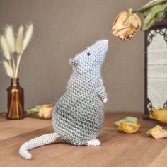 a knitted rat sitting on top of a wooden table next to some dried flowers