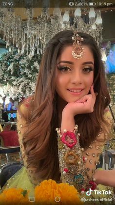 a woman with long brown hair wearing a headpiece and sitting in front of a chandelier