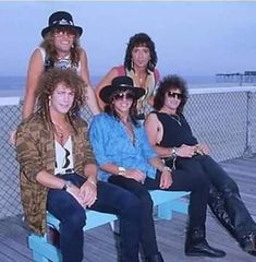 four women sitting on a bench near the ocean with one woman wearing a cowboy hat