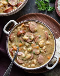 two bowls filled with beans and sausage on top of a wooden plate next to rice