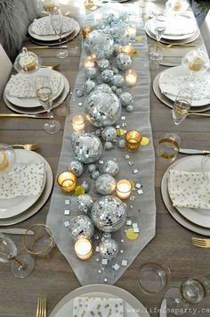 a long table is set with silver and gold christmas balls, candles, and plates