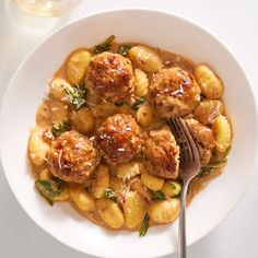 a white plate topped with meatballs covered in gravy next to a glass of wine