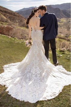 a bride and groom standing in the grass looking at each other with mountains in the background