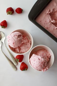 two bowls filled with ice cream next to strawberries