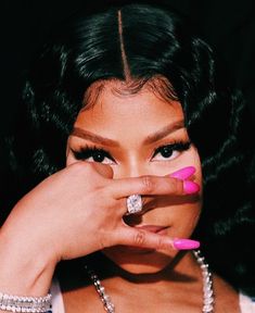 a woman with black hair and pink nails holding her hand to her face while wearing a diamond ring