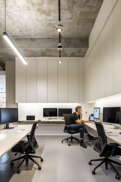 a man sitting at a desk in an office with multiple computer screens on the wall