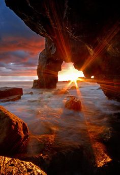 the sun is setting behind some rocks in the ocean with water coming up from them