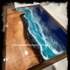 a wooden table with blue water and waves on it's surface in front of a white wall