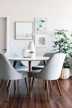 a dining room table with chairs and pictures on the wall above it, along with potted plants