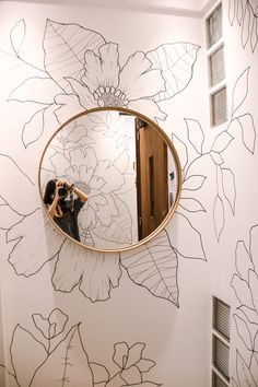 a woman taking a selfie in front of a mirror with flowers painted on it