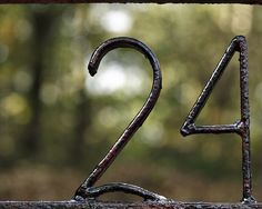 the number twenty four is made out of rusted metal and sits in front of trees