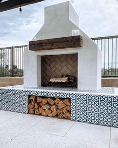 an outdoor fireplace with blue and white tiles on the outside, surrounded by wooden logs