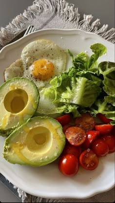 an egg, avocado, tomatoes and lettuce on a white plate