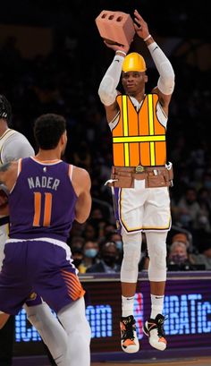 a man in an orange safety vest holding a block above his head while standing on a basketball court