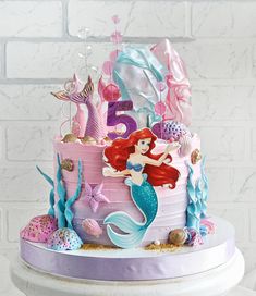 a pink and purple birthday cake with ariel the mermaid on top