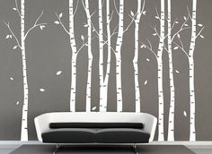 a white couch sitting in front of a wall with trees painted on it's sides