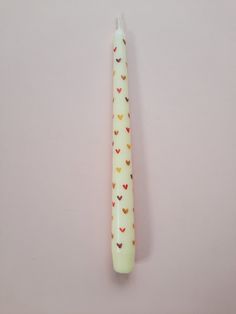 a white candle with hearts on it sitting next to a pink wall in the shape of a heart