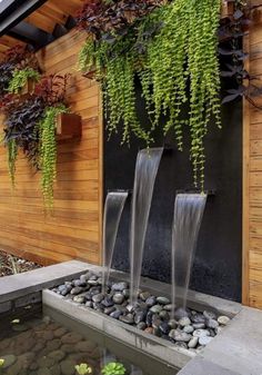 three water fountains in front of a wooden wall with plants hanging from it's sides