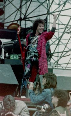 a man on stage with his guitar in the air and some people around him watching