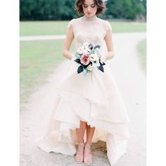 a woman in a white dress holding a bouquet and standing on a path with her hands behind her back