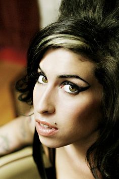 a woman with black hair and piercings on her face looking at the camera while sitting in a chair