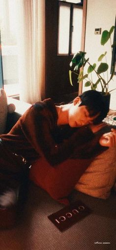 a man laying on top of a couch next to a plant in a living room