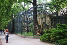 a woman walking down a sidewalk past a zoo enclosure