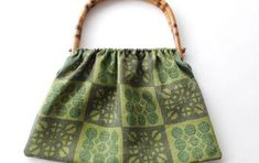 a green purse with wooden handles on a white background, hanging from a bamboo handle