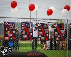 a group of people standing behind a chain link fence with pictures and balloons on it