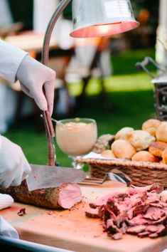 a person in white gloves is cutting meat on a table with bread and other foods