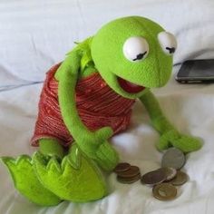 a green stuffed animal sitting on top of a bed next to a cell phone and remote control