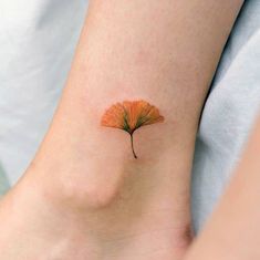 a small leaf tattoo on the ankle is shown in this image, it looks like an orange flower