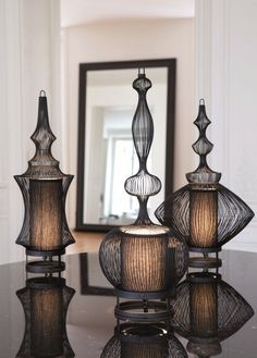 three glass vases sitting on top of a black table next to a framed mirror