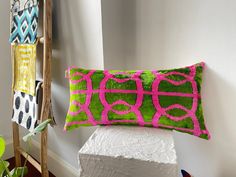 a green and pink decorative pillow sitting on top of a white pedestal next to a ladder