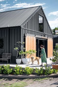 a woman walking her dog in front of a house with black siding and wooden doors