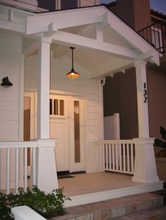 the front porch of a house with white railings and lights hanging from it's ceiling